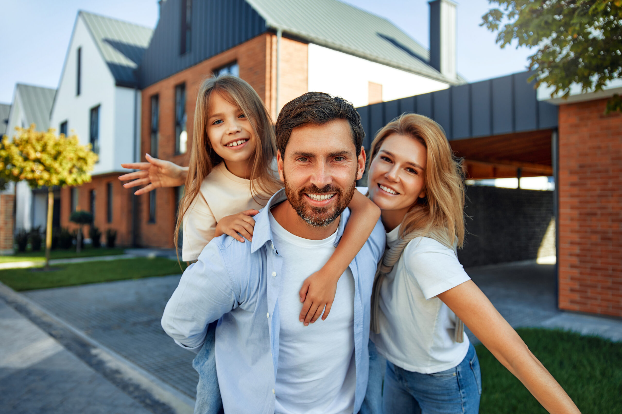 A young happy family with a child hugging each other are standing on the street near their new home. Renting and buying real estate. Moving concept.